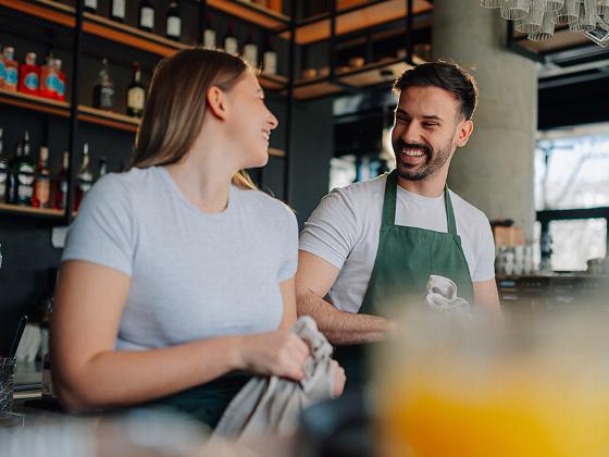two bartenders smiling at each other in a bar setting close up drinks and cocktails in background 3 moments of laughter